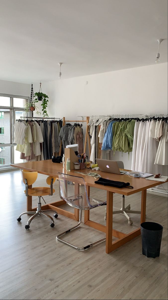 an office space with clothes hanging on racks and a desk in front of the window