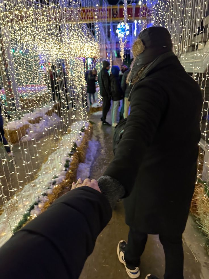 two people are holding hands in front of christmas lights and snow covered walkways at night