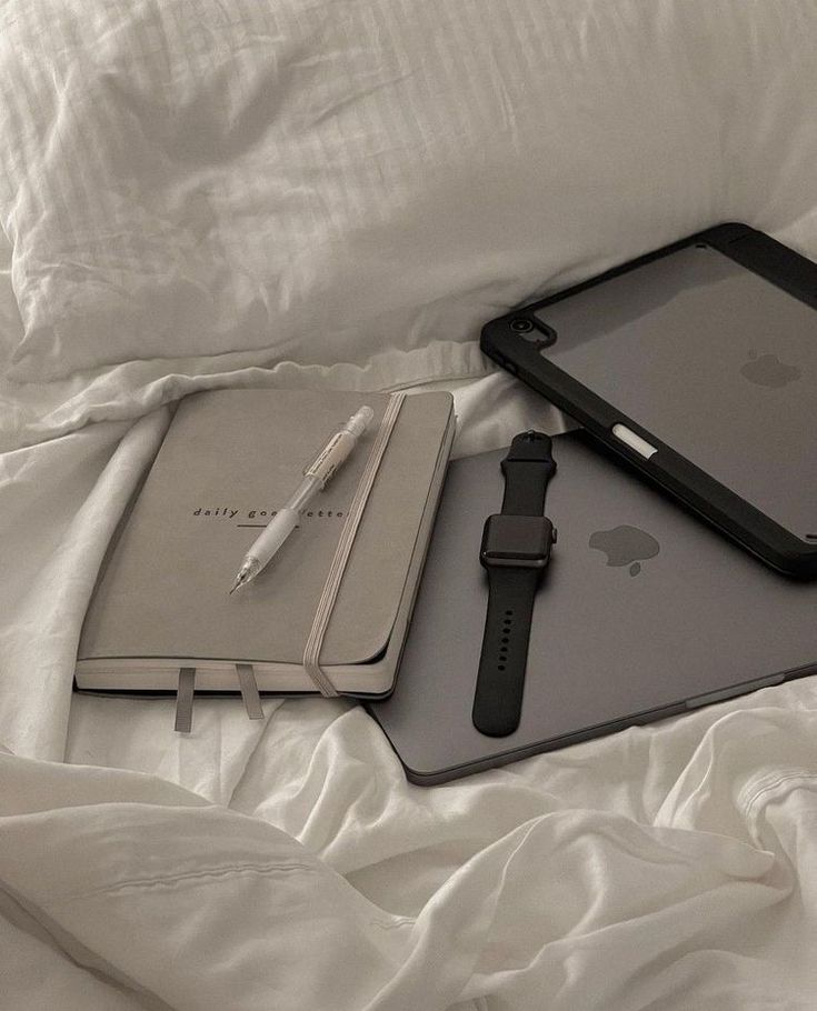 an apple watch, pen and ipad on a bed with white sheets in the background