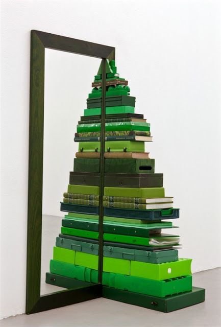 a green christmas tree made out of stacks of books in front of a mirror on the floor