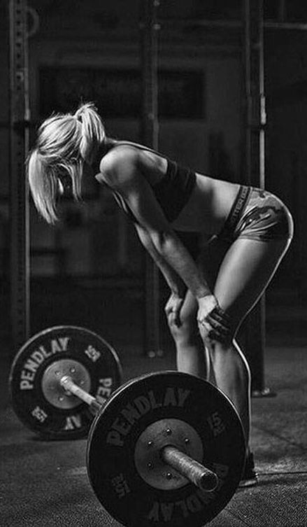 a woman squatting down with a barbell in front of her on the ground