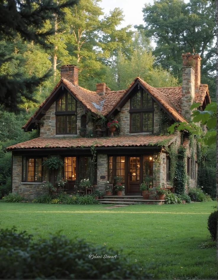 a stone house with lots of windows and plants on the front lawn, surrounded by trees