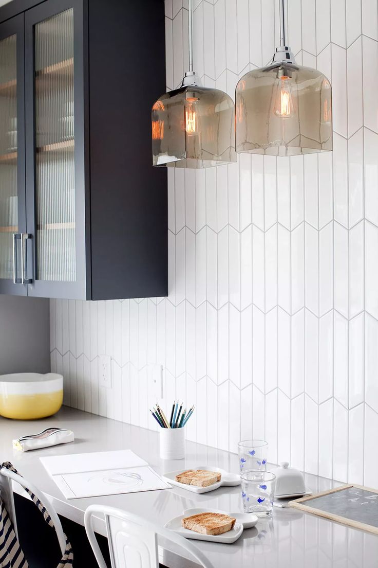 a white kitchen with black cabinets and glass pendant lights over the counter top, along with plates on the table