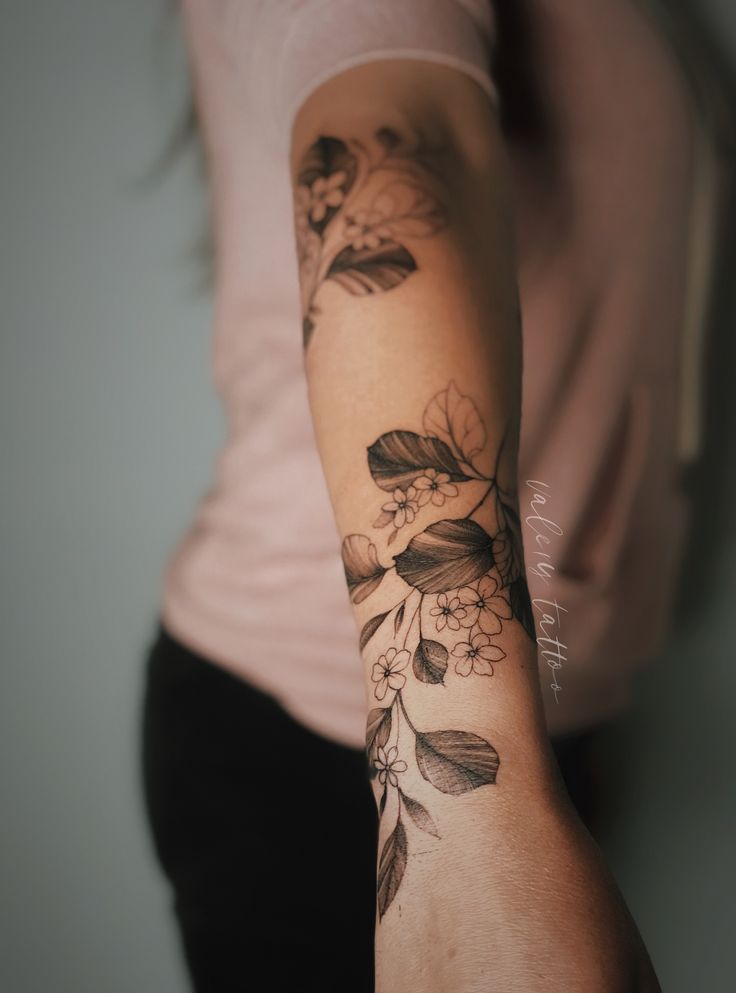 a woman's arm with flowers and leaves tattooed on the left side of her arm