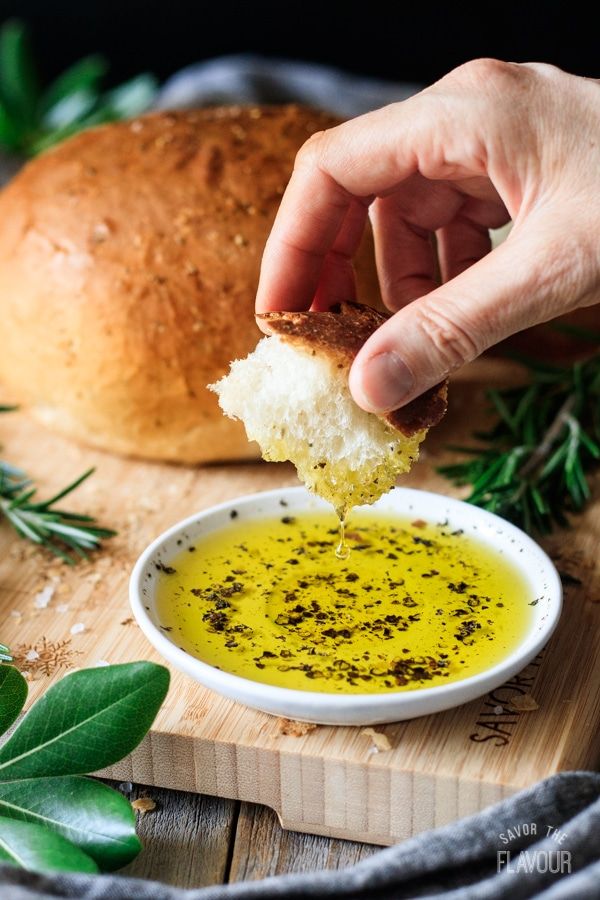 a person dipping some bread into a bowl of olive oil on top of a cutting board