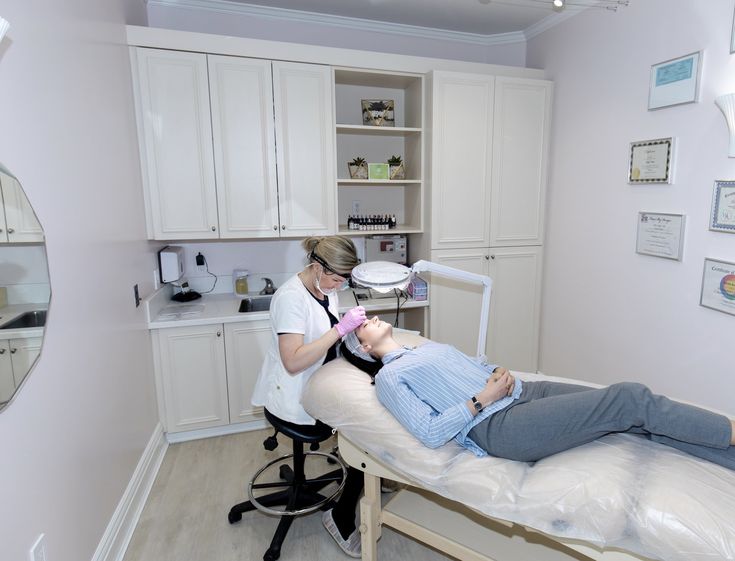 a woman getting her teeth brushed by a dentist in a room with white cabinetry