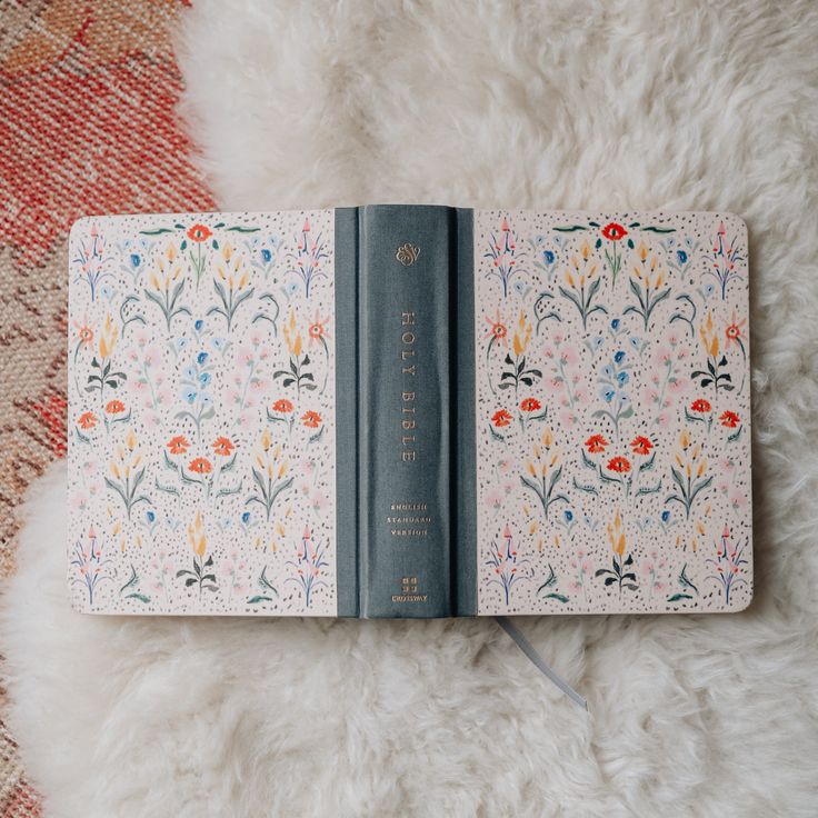 an open book with flowers on it sitting on top of a fluffy white rug next to a knife