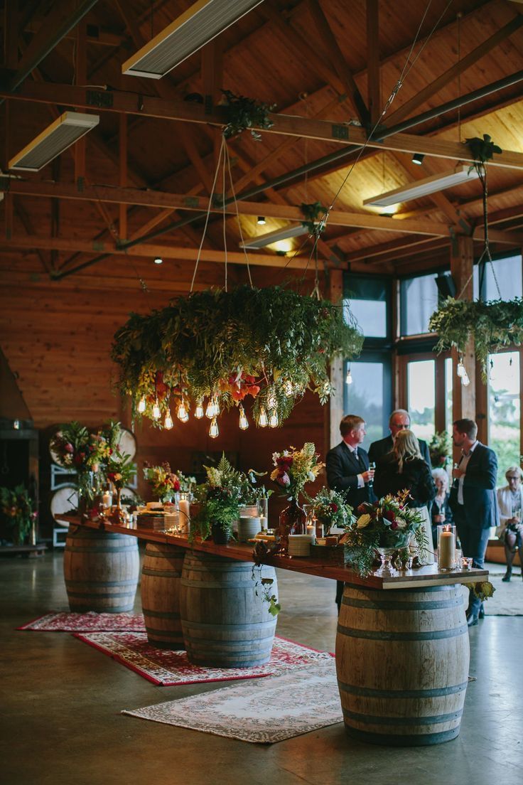 people are standing around in a large room with wooden barrels and plants hanging from the ceiling