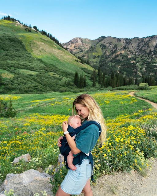 a woman holding a baby in her arms while walking through a field full of wildflowers