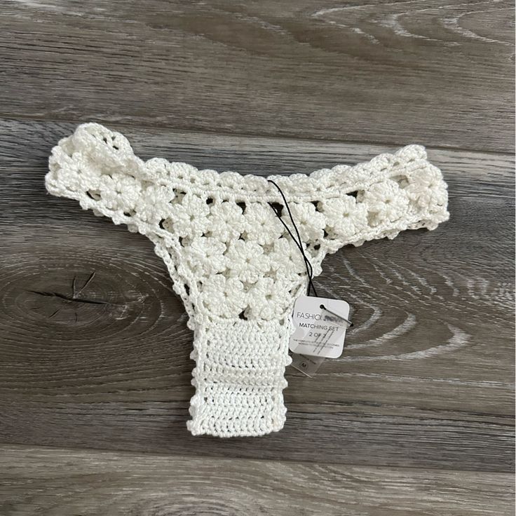 a white crocheted baby sweater on a wooden floor with a tag attached to it