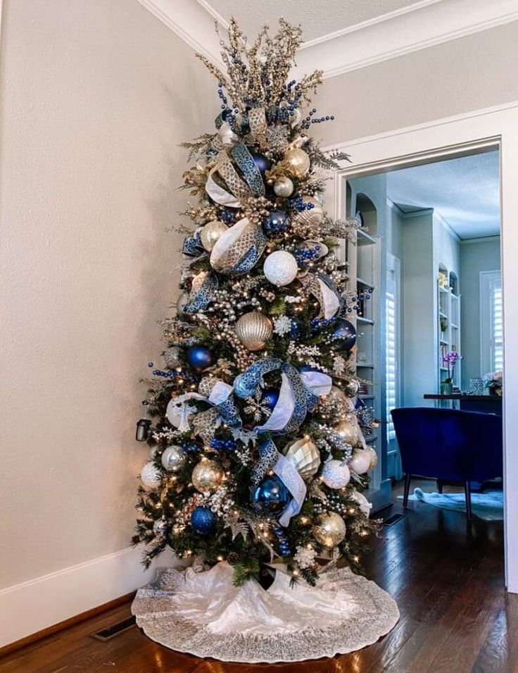 a decorated christmas tree with blue and silver ornaments in a living room next to a doorway