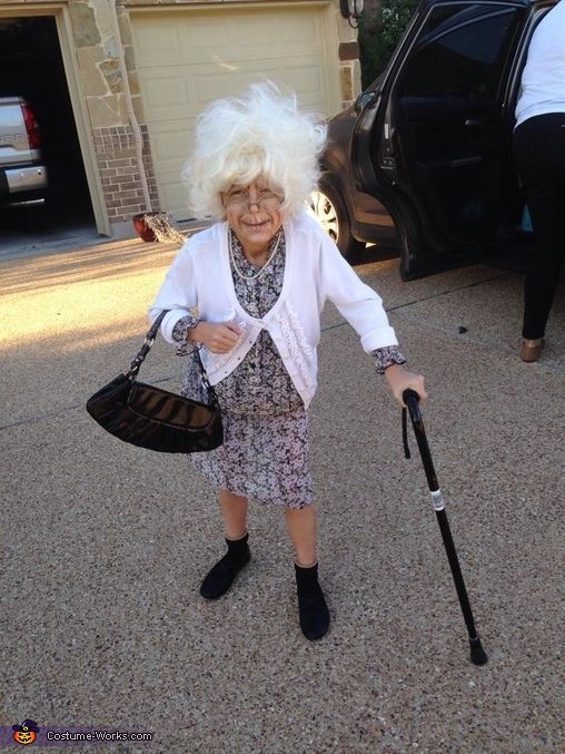 an older woman with white hair holding a cane and walking in front of her car