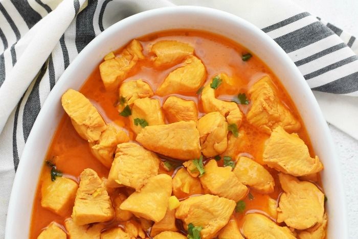 a white bowl filled with chicken curry and garnished with cilantro leaves