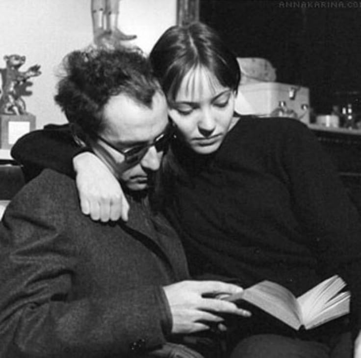 a man and woman sitting on a couch looking at an open book