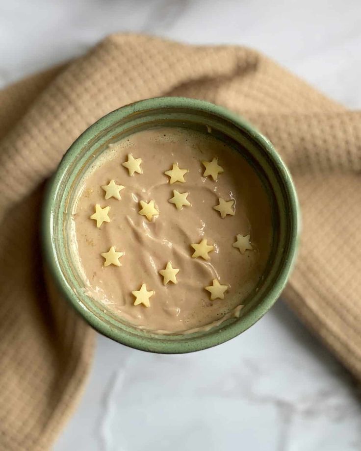 a green bowl filled with food on top of a white tablecloth and gold stars