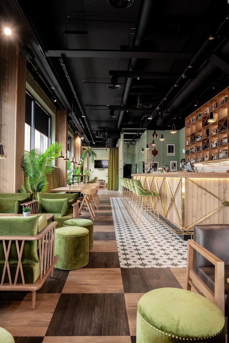 the interior of a restaurant with checkered flooring and green velvet chairs, stools, and wooden shelves