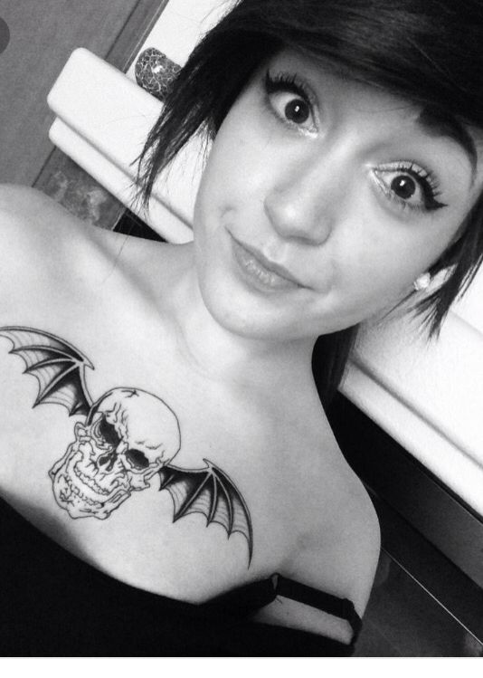 a woman with a skull and bat tattoo on her chest is looking at the camera