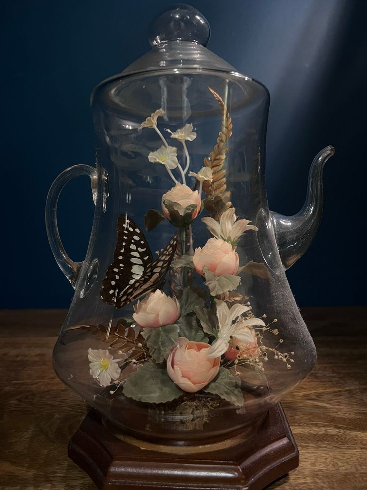 a glass teapot with flowers and a butterfly in it