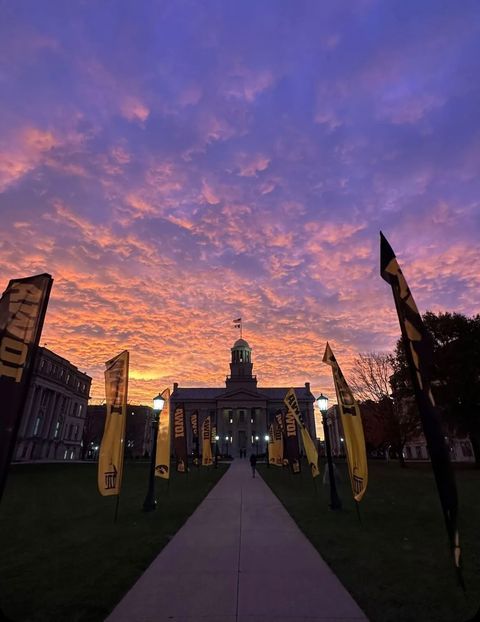 the sun is setting over an old building with flags in front of it and a clock tower