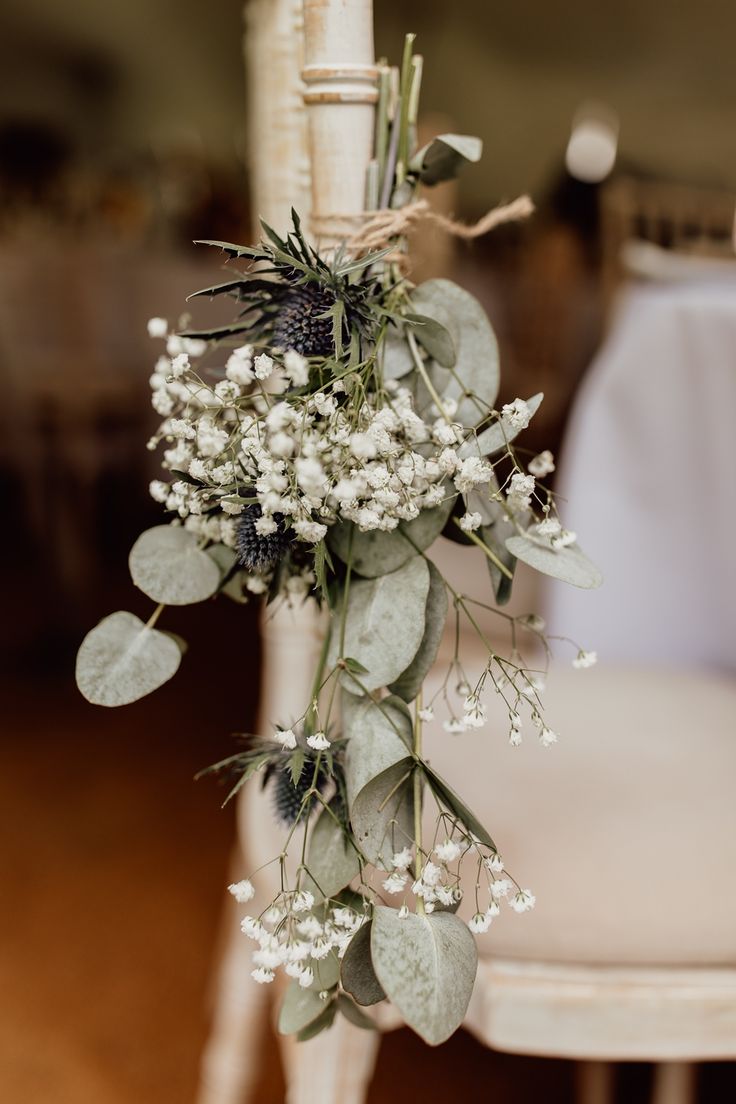 flowers and greenery are hanging from the back of a chair at a wedding reception