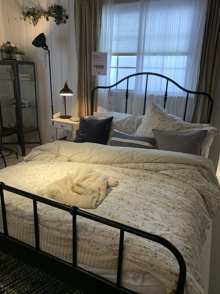 a bed with white sheets and pillows in a bedroom next to a lamp, dresser and window