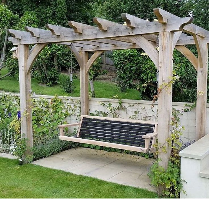 a wooden bench sitting under a pergoline covered arbor in a garden area with flowers and greenery