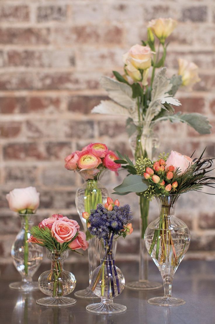 three vases filled with different types of flowers on a table next to a brick wall