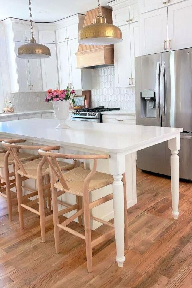 a kitchen with white counter tops and wooden chairs in front of an island that has four stools on it