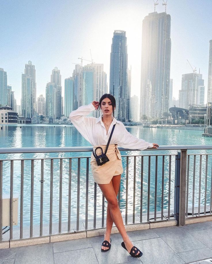 a woman is standing on a bridge in front of the water with her hands behind her head