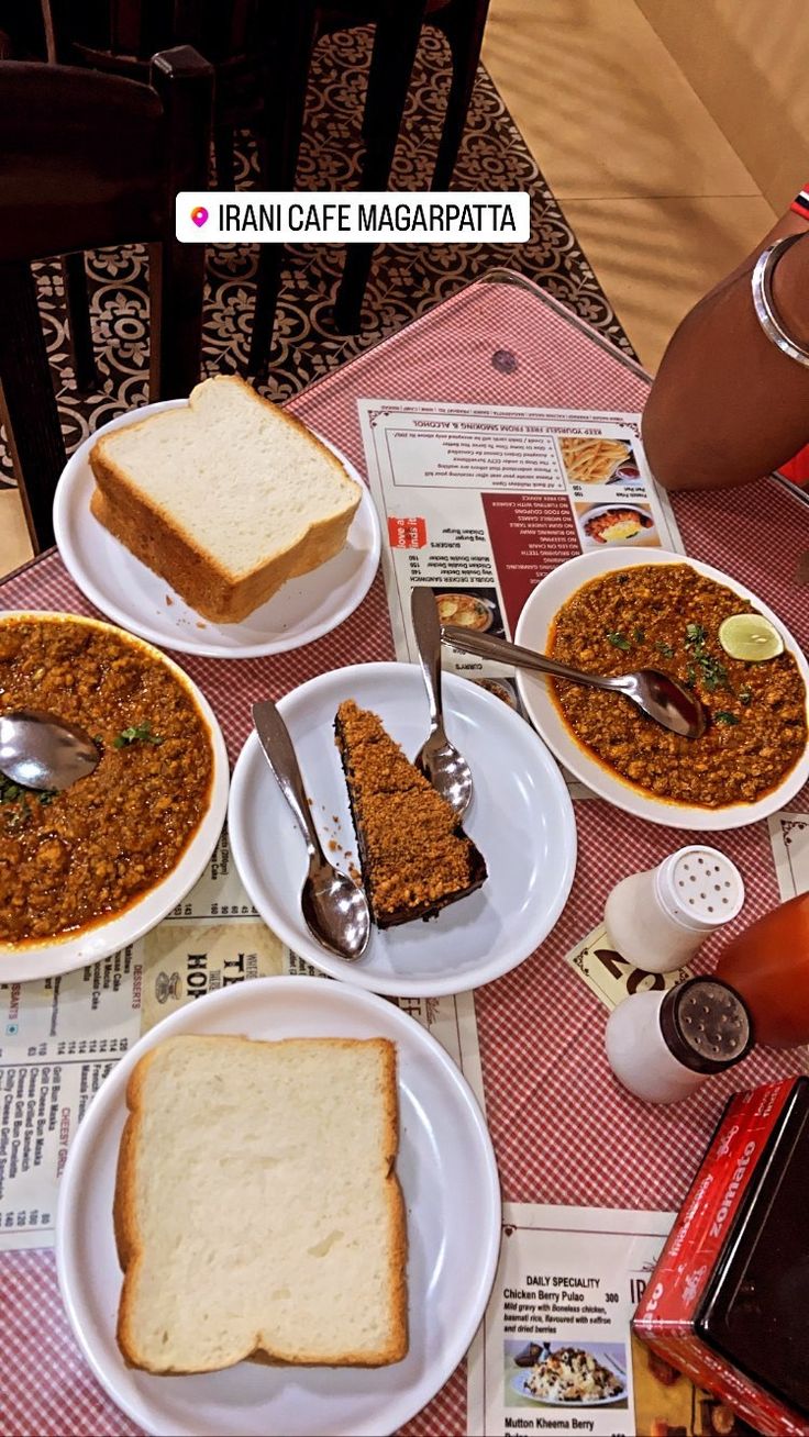 a table topped with plates of food next to a cup of coffee and spoons