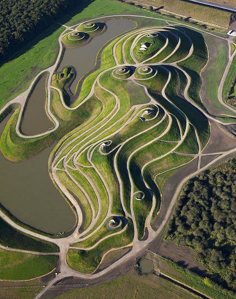 an aerial view of a green landscape with water and trees in the foreground, surrounded by grass mounds