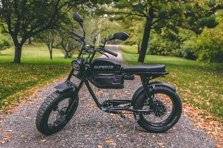 a black motorcycle parked on the side of a road in front of trees and grass