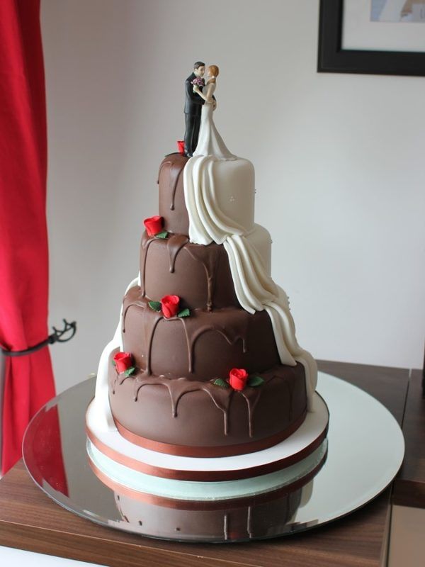 a wedding cake with chocolate frosting and red roses on top is sitting on a table