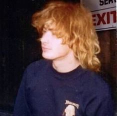 a young man with red hair standing in front of a sign