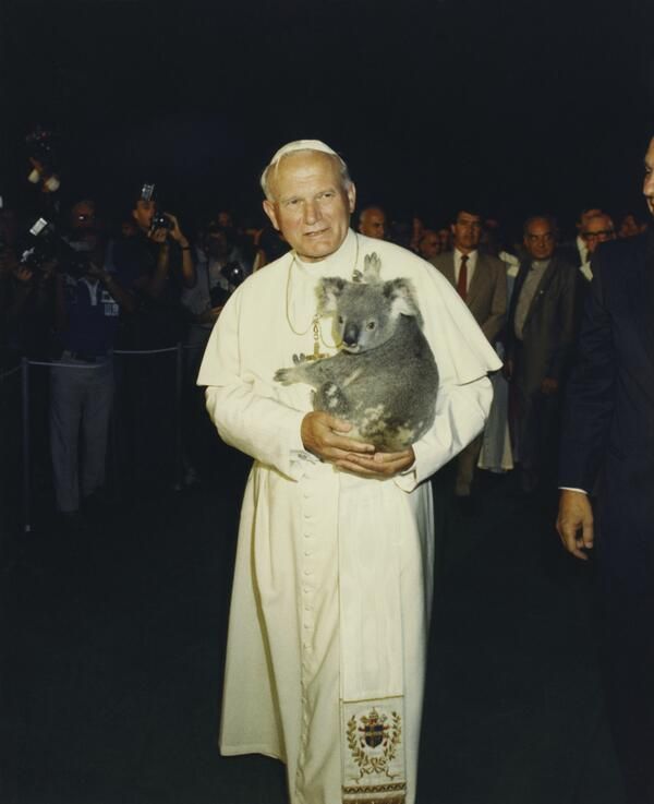 a man holding a koala bear in his arms while standing next to other people