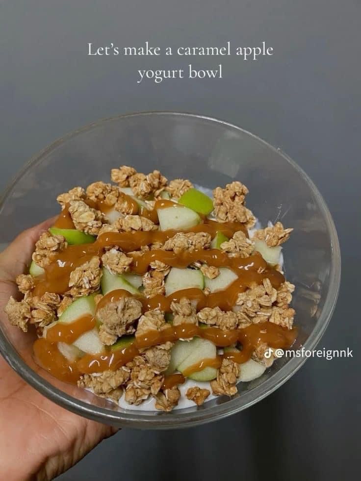 a bowl filled with granola, apples and yogurt in caramel sauce