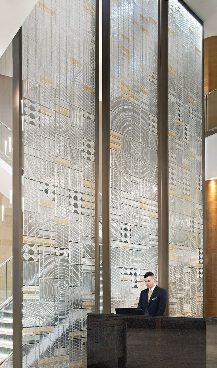 a man sitting at a desk in front of a large glass wall with intricate designs on it