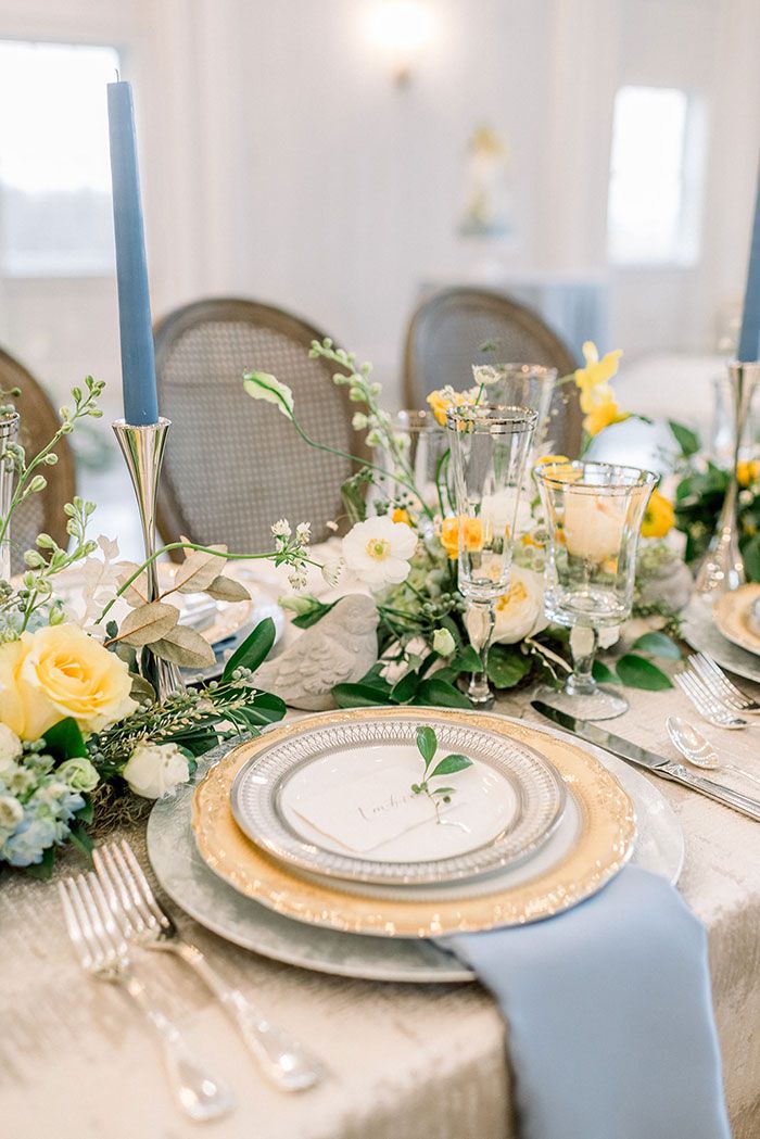 the table is set with yellow and white flowers, silverware, and blue candlesticks