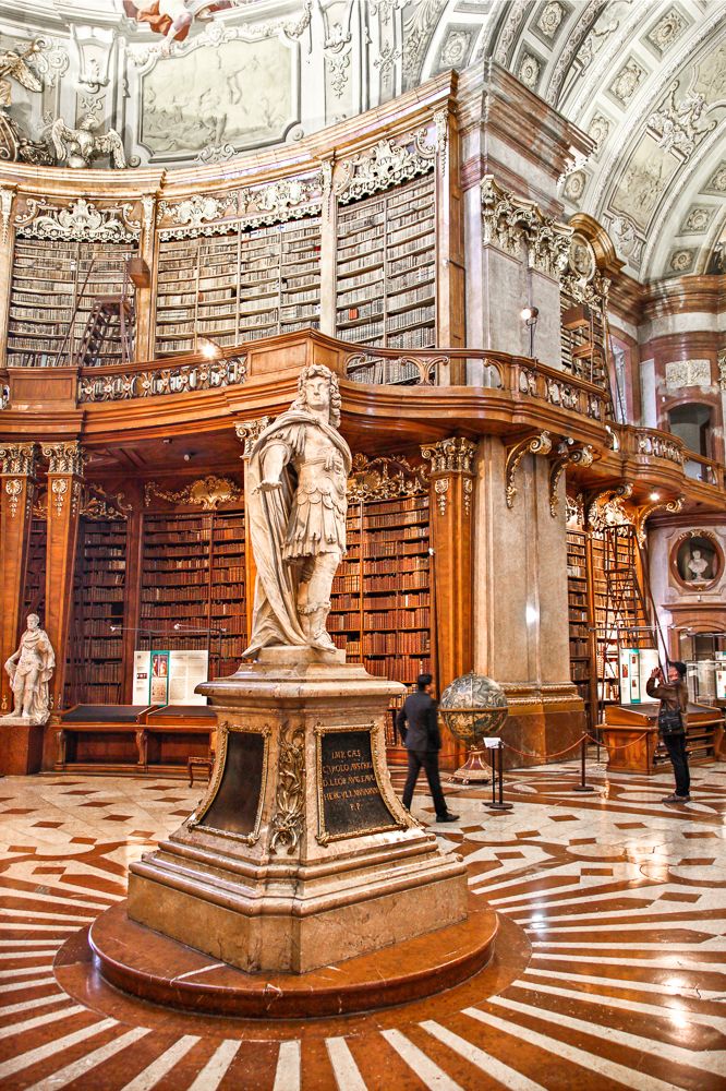 the inside of a large library with many bookshelves and statues on it's walls