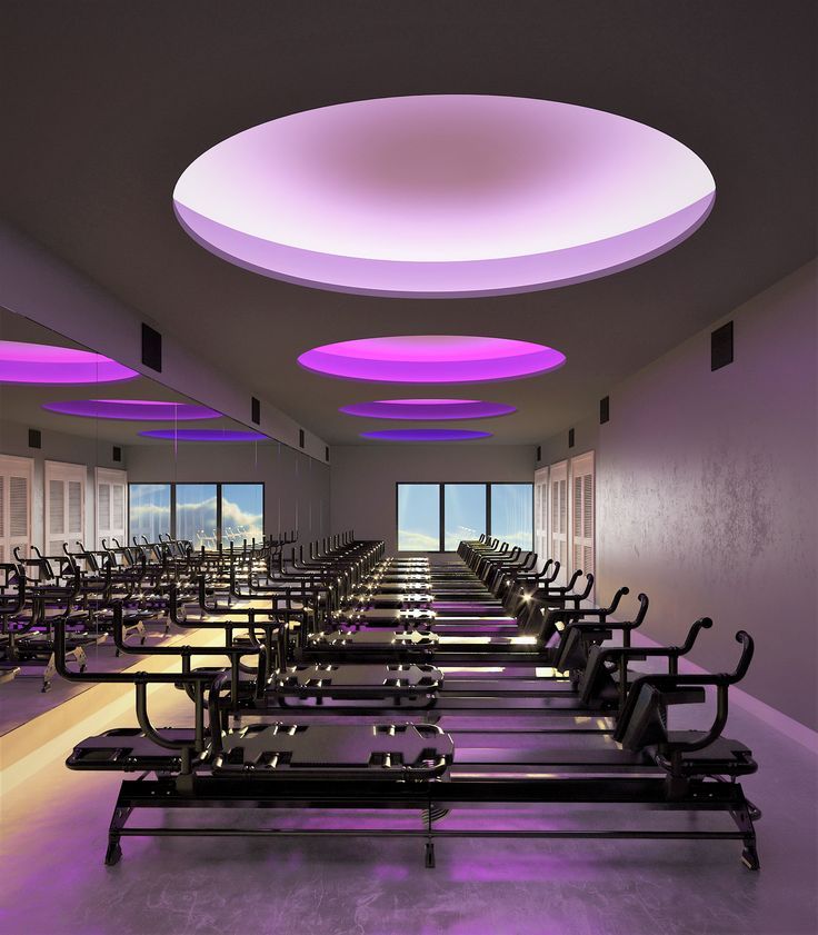 rows of treadmills in a gym with purple lighting on the ceiling and large windows