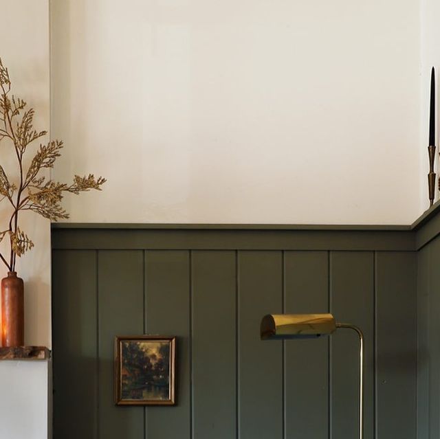 a bathroom with green painted walls and wood paneling on the wall, along with a gold toilet paper dispenser