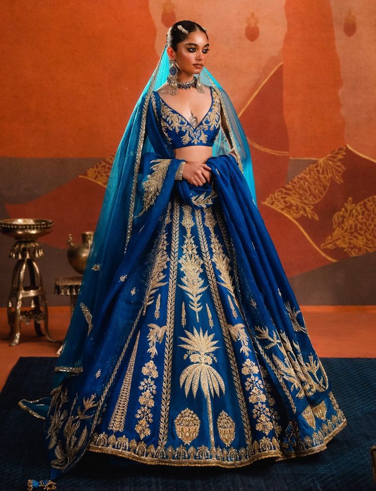 The neel bahar lehenga in brilliant azure blue sparkles at any occasion. Adorned with delicate sehra motifs that shimmer throughout, it is paired with a sleeveless embellished blouse and a long tulle dupatta. Featuring hours of artisanal handwork with zardozi, katdana, and sitara embroidery, this lehenga is a modern-day fairytale. It also includes a separate cancan. Blue Cutdana Sharara For Festive Occasions, Festive Blue Sharara With Cutdana, Designer Blue Sharara With Zari Work, Blue Cutdana Designer Wear Sets, Blue Unstitched Cutdana Sets, Elegant Blue Cutdana Sets, Blue Sharara For Diwali Festivities, Blue Sharara For Navratri Festival, Blue Sharara For Navratri Festivities