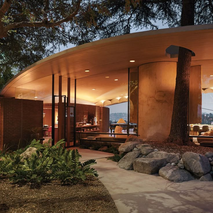 a circular building with trees and rocks in the foreground at night, lit up by lights