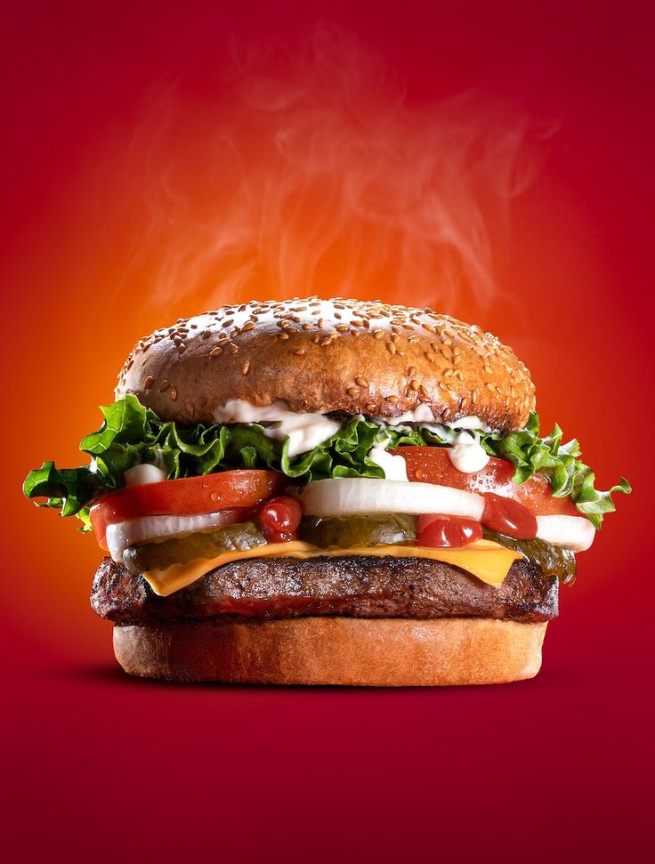 a hamburger with cheese, lettuce and tomato on it in front of a red background