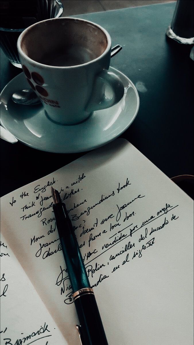 a pen sitting on top of an open notepad next to a cup of coffee