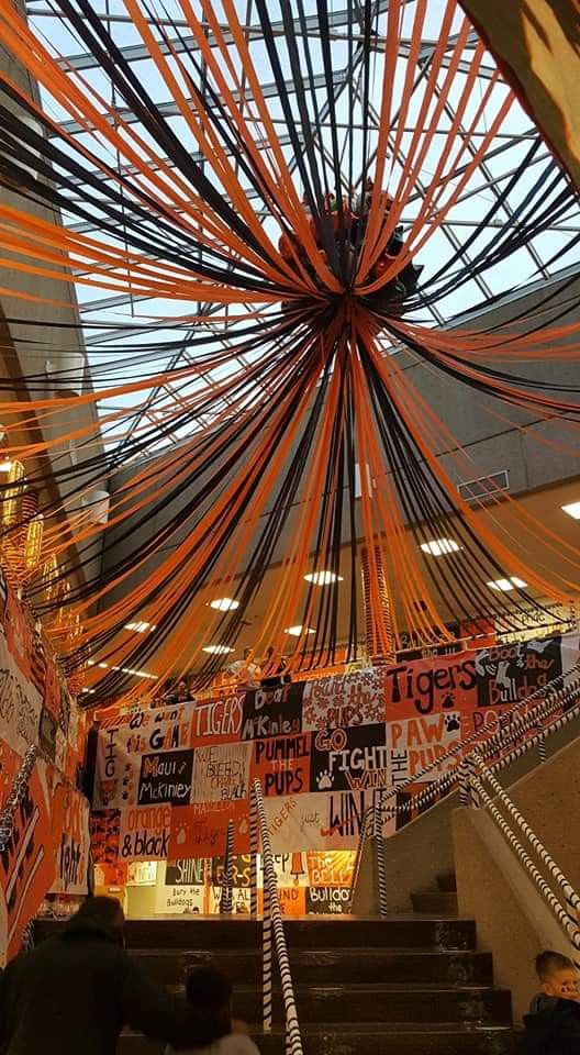 the ceiling is decorated with orange ribbons and banners for an upcoming event or celebration, as well as several people walking up stairs