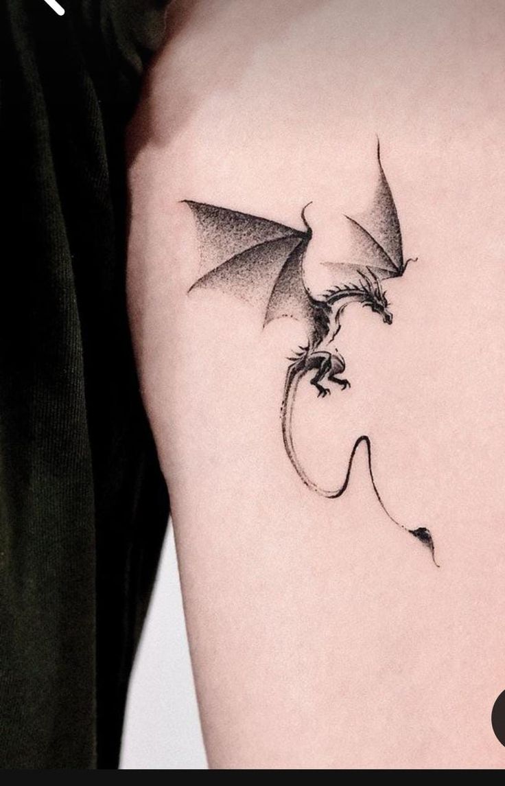 a small dragon tattoo on the left side of the right arm, with its wings spread out