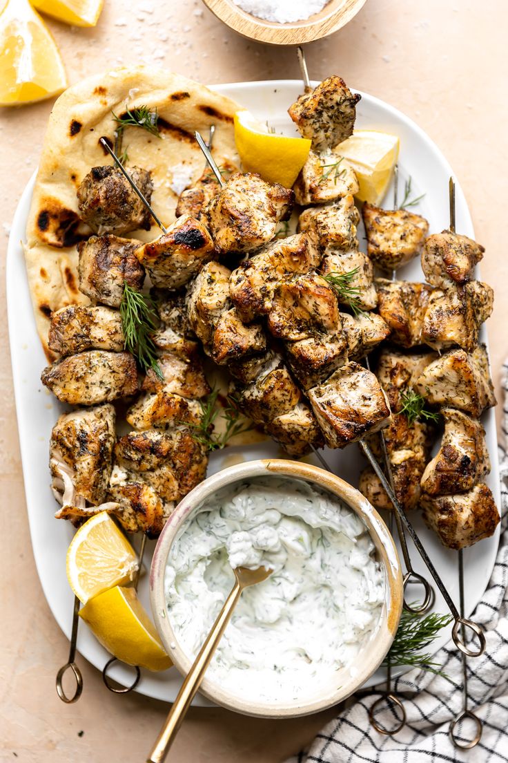 grilled chicken skewers with tzatzh and lemon wedges on a white plate