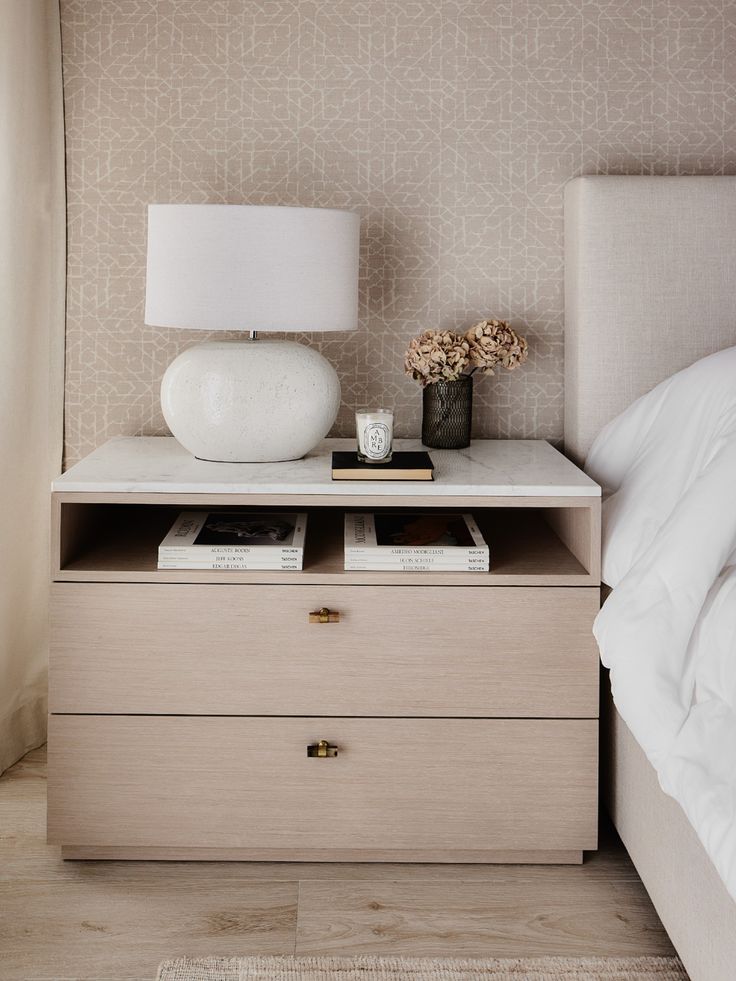 a nightstand with two drawers and a lamp on top of it next to a bed