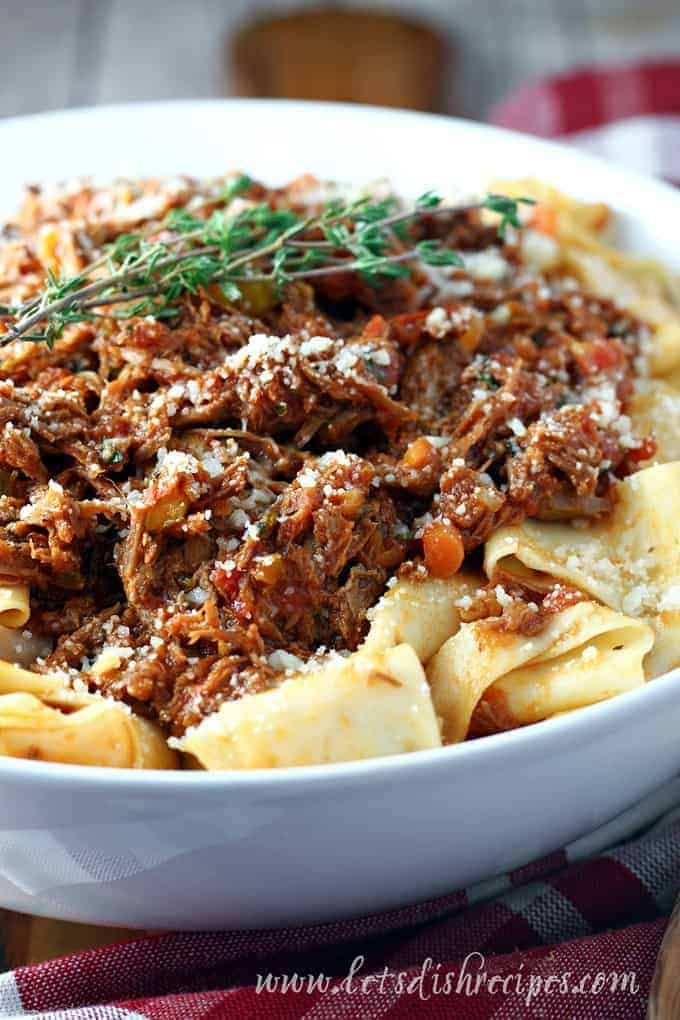 a white bowl filled with pasta covered in beef ragu and topped with parmesan cheese